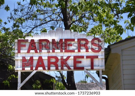 Rustic fence design, completed with white weathered boards, has farmers market spelled out in red letters.