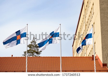 Three finnish national flags with coat of arms on the wind against the blue sky