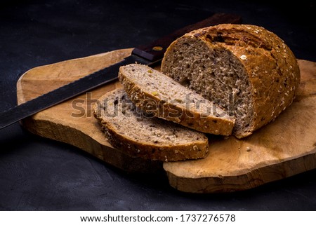 Loaf of bread with knife on wooden board. Dark background