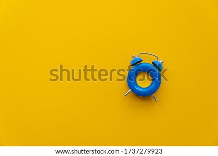 Vacation time. Blue alarm clock as swimming ring form on yellow background. Top view. Copy space
