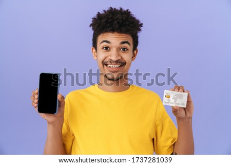 Photo of smiling african american man showing credit card and cellphone isolated over purple background