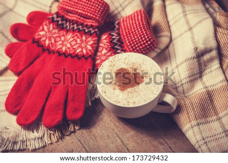 Cup with coffee and shape of the cacao heart on it and scarf. Photo with focus on heart.