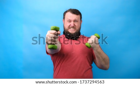 Thick bearded nice bodybuilder in pink T-shirt with very small dumbbells is very tense doing exercises on a blue background