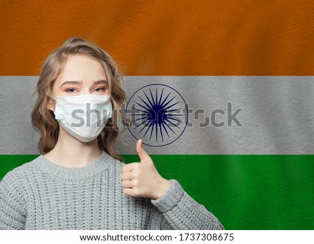 Happy woman in face mask holding thumb up on national indian flag background. Flu epidemic and virus protection concept