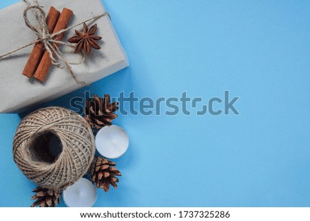 Christmas layout on blue background, top view. Flatley, Packed in craft paper, tied with string with cinnamon sticks and anise. Candles and cones create comfort in cold, decor.