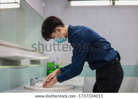Man is standing and washing his hands in the bathroom, The male office worker wears a mask and is cleaning hands in the bathroom. Royalty-Free Stock Photo #1737334013