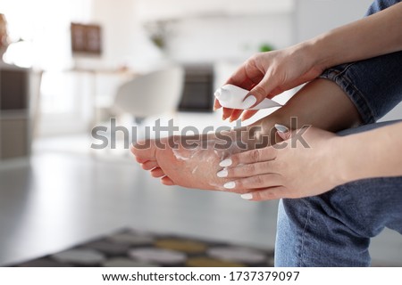 Tired woman using pain relief cream for foot after fatigue, long walking, working, standing, flat feet or injury, sitting indoors. Suffering from hurt of arch, ball, heel or toe treatment