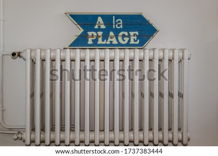photograph of an old white metal radiator with a blue sign indicating where the beach is