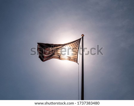 Photograph of the United states of america flag with the sun behind and a big blue sky