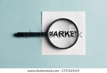 MARKET word inscription on a white sticker on blue table with magnifying glass loupe. Market concept