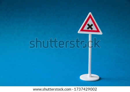 Road sign, plastic triangular red road sign crossing equivalent roads. On a blue background.