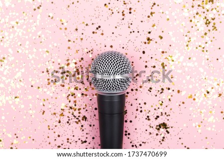 A microphone on pink background decorated with confetti. Minimal compostion.