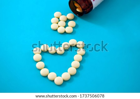 Heart of yellow pills on a blue background. Scattered eight yellow tablet and part of a glass jar over it