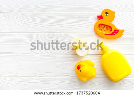 Bath accessories for kids. Yellow rubber duck,towel, cream, shampoo on white wooden background top view