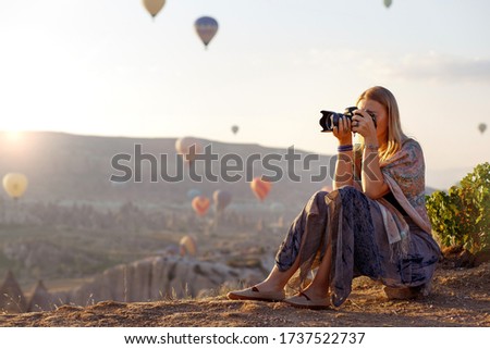 Woman photographer takes pictures of flying hot air balloon at dawn in Cappadocia, Turkey. Travel concept.  Dressed in a scarf with a Turkish national pattern Ebru