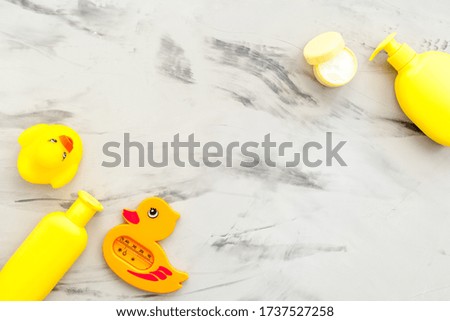 Baby care. Bath cosmetics and toy for child. Shampoo, gel, cream, towel. Gray marble background top view copyspace

