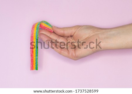 Long marmalade chewing candy in sugar, colors of the rainbow in the hand. LGBT symbol. Sweets on pink background