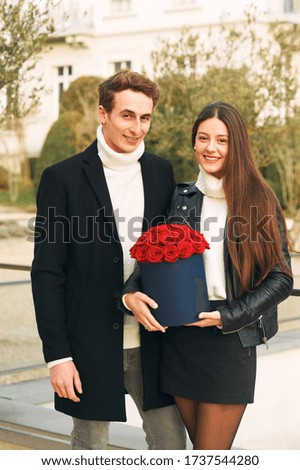 Happy laughing couple, man offering flower box of red roses to beautiful young woman