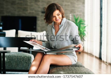 Young happy woamn looking at photo album, resting in cozy living room Royalty-Free Stock Photo #1737547607