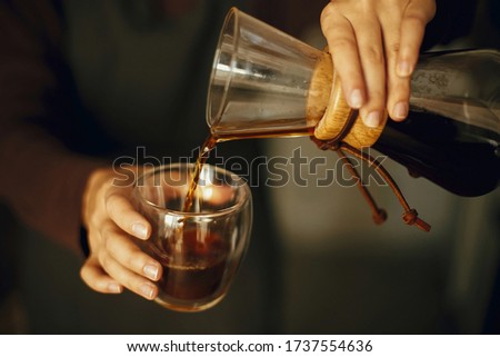 Professional female barista in black uniform making drip coffee. Person pouring fresh aromatic coffee from glass flask in cup, hands close up. Alternative coffee brewing. Royalty-Free Stock Photo #1737554636