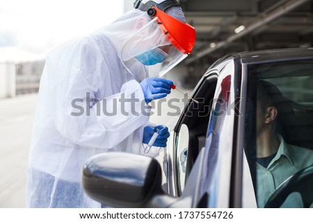 Medical worker in PPE performing nasal  throat swab on person in vehicle through car window,COVID-19 mobile testing centre,drive through facility parking lot,specimen collection and rt-PCR diagnostic