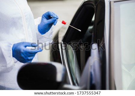 Medical worker in N95 PPE performing nasal throat swab on person in vehicle through car window,COVID-19 UK mobile testing centre drive thru facility,hands closeup in blue gloves holding test kit Royalty-Free Stock Photo #1737555347