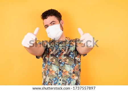 Young beautiful businessman with short hair and piercing wearing casual hawaiian shirt approving doing positive gesture with hand, thumbs up smiling and happy for success. Winner gesture.