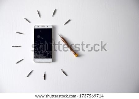 White broken cell phone surrounded with screwdrivers on white background