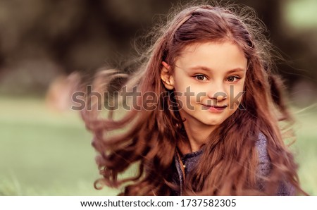Happy smiling kid girl waving long hair on summer grass background. Closeup toned color
