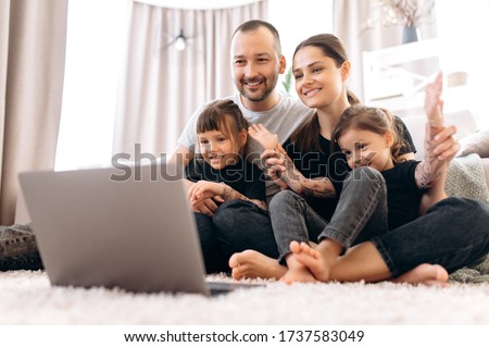 Good time. Video call. Family leisure at home. Happy family is chatting with grandparents by video conference on laptop sitting at home on the floor