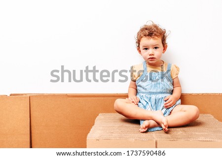 Portrait of 1 year old girl with white background, playing on some cardboard, copy space.