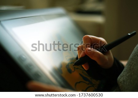 digital artists hand using graphics tablet. Majority of image is out of focus/bokehish apart from the hand, pen and some of the screen