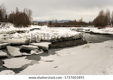 Winter landscape with ice breaking, cracking and melting from a frozen creek / river in the north of Anchorage, Alaska. Taken next to Ship Creek Overlook Park. Mountains of Chugach Park in the back. 