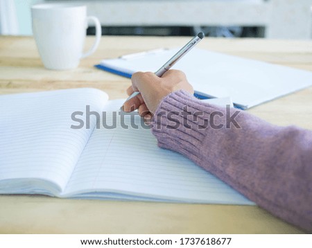 Hand woman writing on book with wood background. work at home concept.