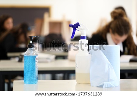 Deliberately blurred students in the background working on classwork. Hand sanitizer sanitiser pump with disinfectant spray bottle in the foreground. Corona virus Covid 19 education school theme.  Royalty-Free Stock Photo #1737631289