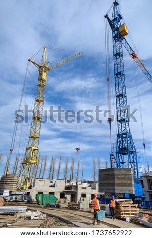 House construction. Photos of high-rise construction cranes and an unfinished house against a blue sky. Photographed from the bottom up on a wide angle lens