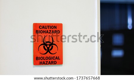 The Caution sign "Biological Hazard” for warning inflected biohazard area, a safety sign warning on white wall in laboratory room, useful for caution who working in microbiology medical science room. Royalty-Free Stock Photo #1737657668