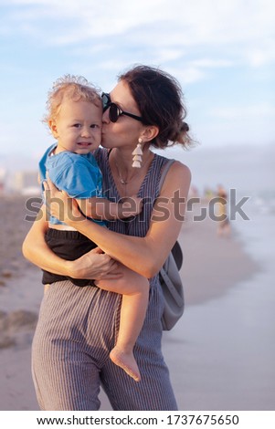 Portrait of adorable toddler boy with his beautiful mother. Mother kissing her child. Mom and son walking on the beach, Family on the ocean vacations.
