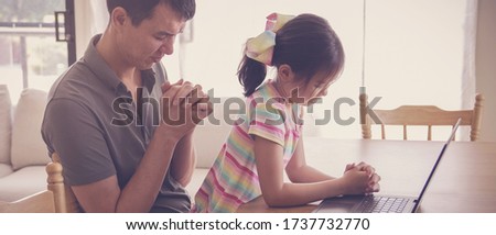 Young girl praying with father parent with laptop, family and kids worship online together at home, streaming church service, social distancing concept