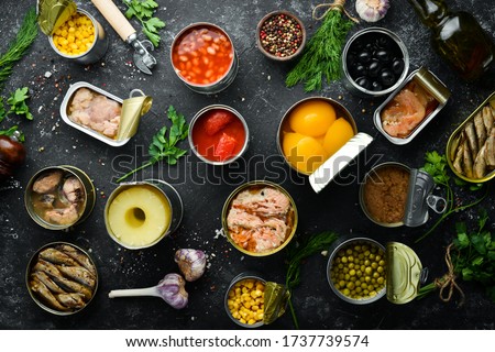 Canned vegetables, beans, fish and fruits in tin cans on black stone background. Food stocks. Royalty-Free Stock Photo #1737739574