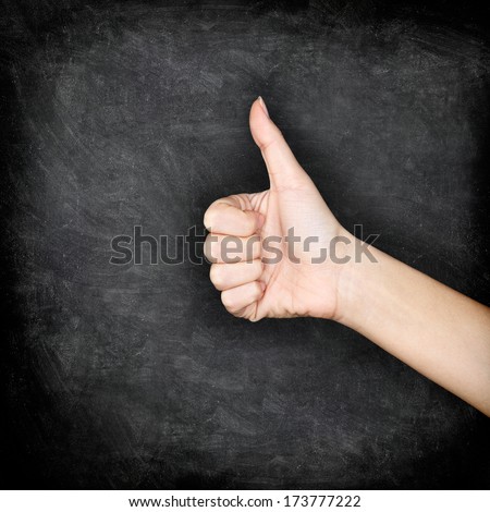hand giving thumbs up on blackboard. Close up of thumbs up hand sign gesture of approval on chalkboard texture background.