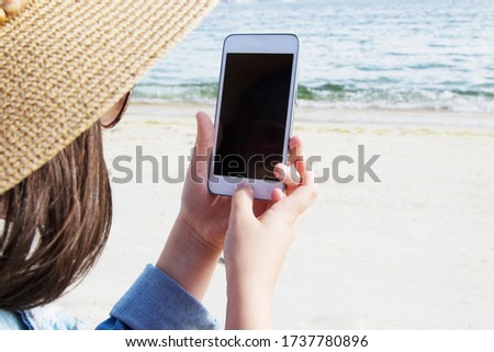 girl in hat and denim jacket using mobile phone on the beach