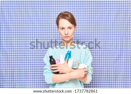 Portrait of serious girl with anti-acne skincare product on face, holding many cosmetic bottles, jars and vials, over shower curtain background. Care for imperfect acne-prone skin. Beauty concept