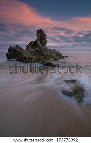 stone on seashore at sunset with a wave