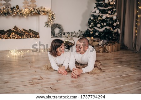 Lovers lie on the floor near the fireplace and Christmas tree