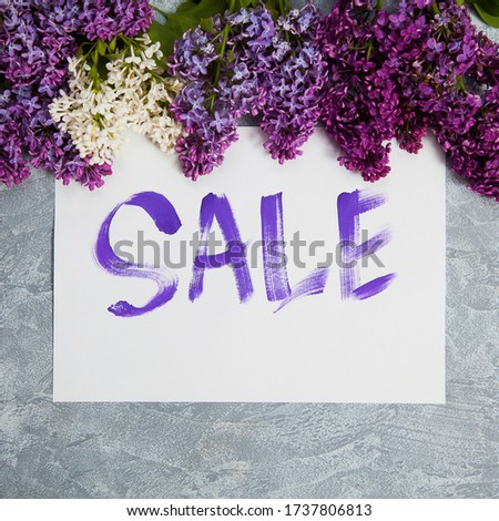 Handwritten word sale in white frame lay in lilac blossom. Shopping concept.