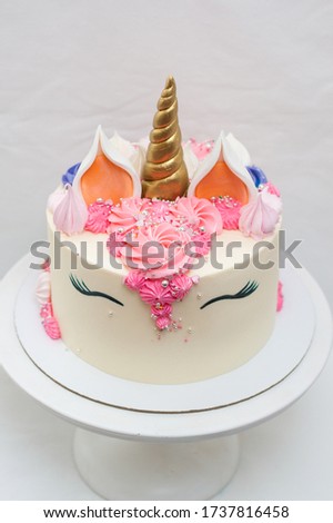 Homemade unicorn layered cake decorated with pink whipped cream. Light grey plain background.