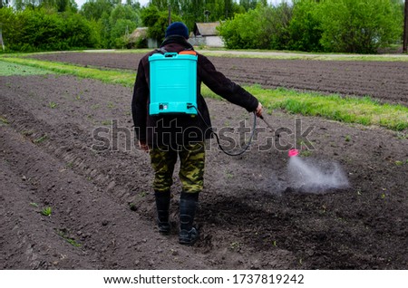 A farmer sprays insecticides or pesticides to control insects in the field using a poison machine. Farmer fighting insects and weeds Royalty-Free Stock Photo #1737819242