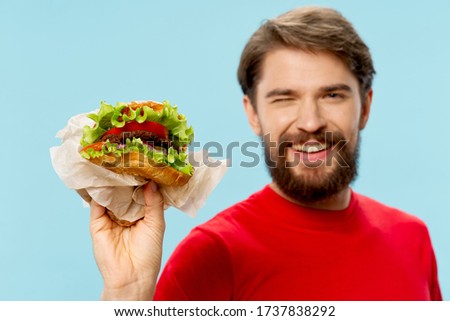 A man in a red t-shirt with a hamburger smiles at the camera