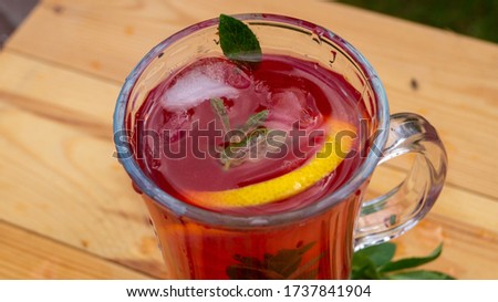glass goblet with cold cocktail on a wooden table in the garden on a background of green plants